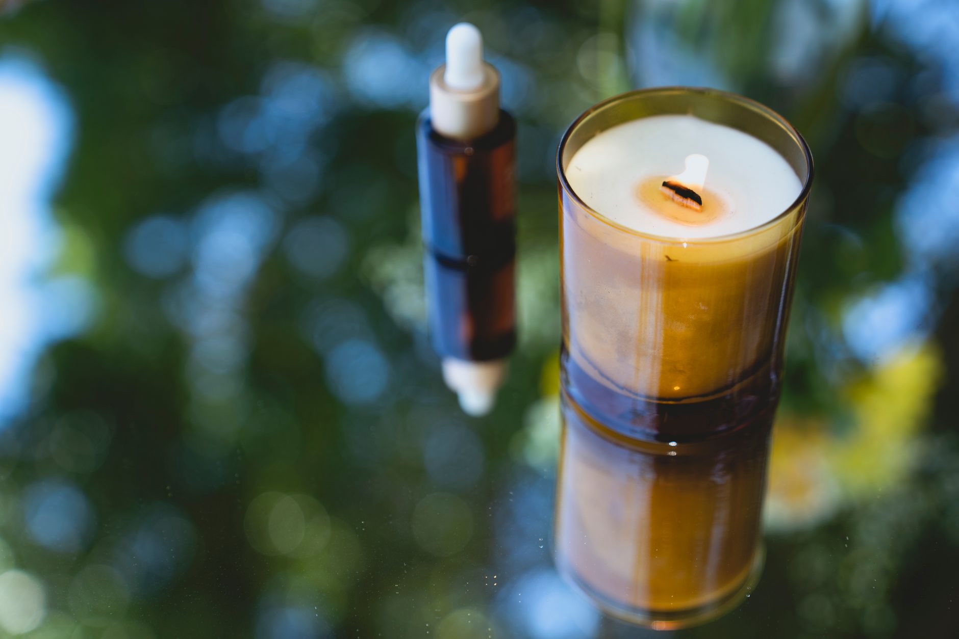 Small amber bottles of essential oil arranged beside a lit candle on a table
