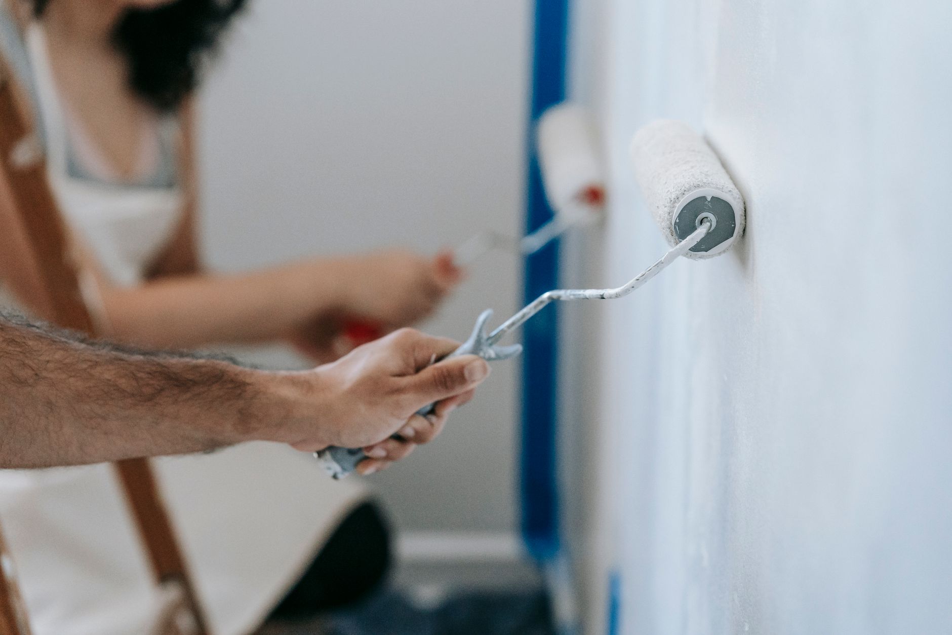 a person rolling pale paint onto an interior wall in a bright room